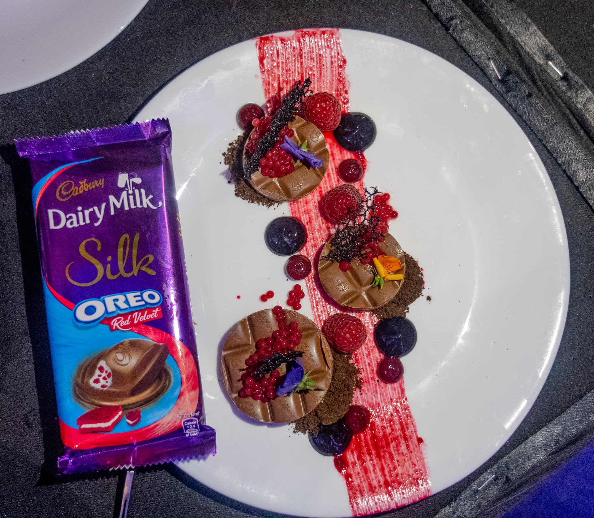 Close-up of a plated gourmet dessert with berries and chocolate beside a full bar.