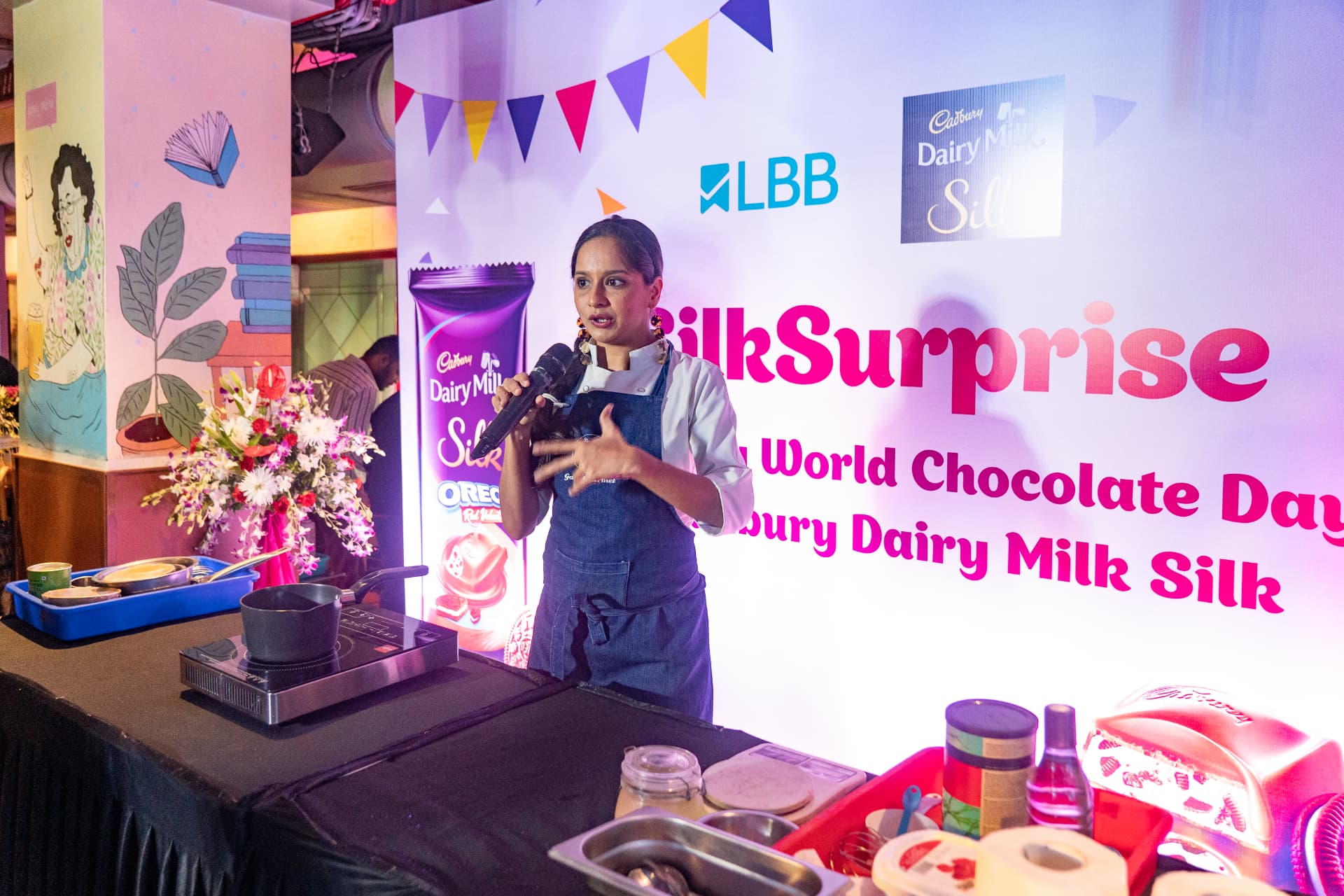 Chef speaking into a microphone behind a cooking demo table at the Cadbury Silk launch.